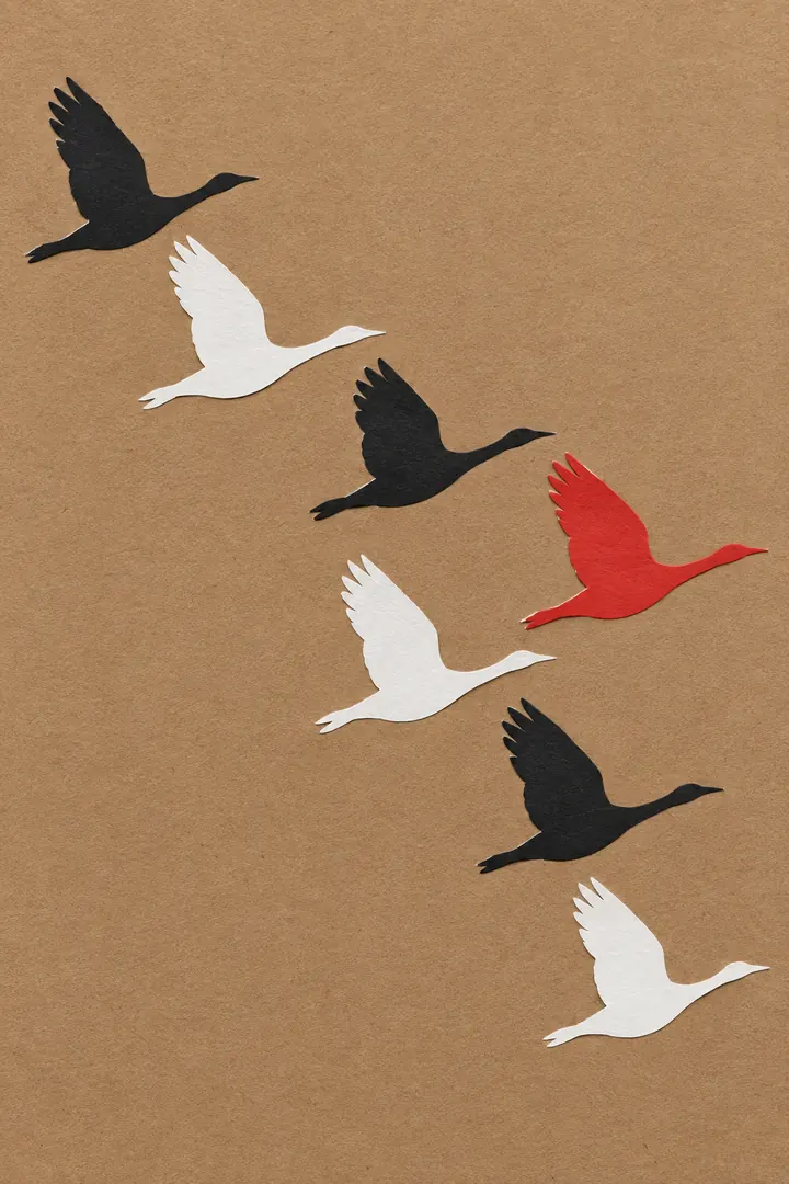 Cut-paper collage of seven geese flying in a diagonal line across brown kraft paper, in black and white with one red goose